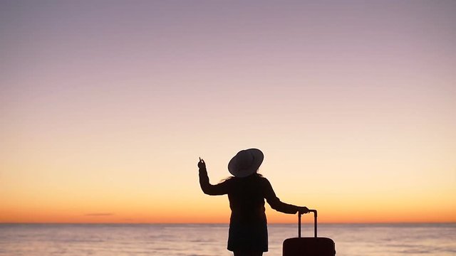 Silhouette of a woman with a suitcase on the beach at sunset