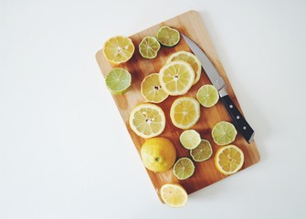 Lemon and lime cuts on a wooden board with a knife on a side. Citrus variety on a white background. Vitamins, summer, freshness. Top view, copy space.