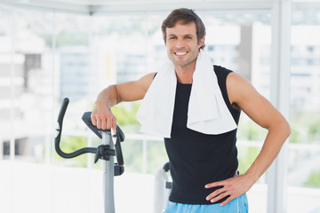 Fototapeta na wymiar Smiling man standing at spinning class in bright gym
