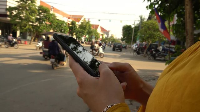 4K Asian woman using mobile phone on street with traffic cars in Siem Reap. Girl using smartphone on city of cambodia. A tourist using device phone. People travelers check smartphone-Dan