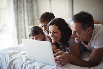 Fototapeta premium Happy family using laptop on bed in bedroom