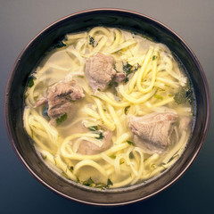 Soup noodles with meat in a plate on a dark background close-up