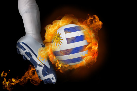 Football player kicking flaming uruguay ball against black