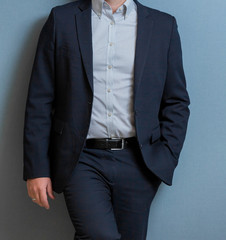 Cropped head Man standing in a smart suit with one hand in his pocket against a blue wall