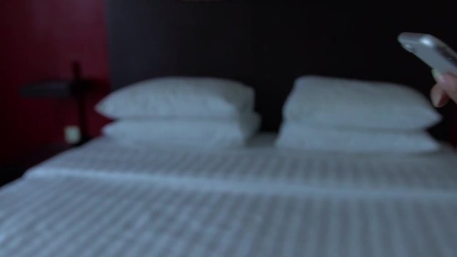 Slow Motion of Asian woman hold in hands the phone device in the hotel room with white sheets on the bed. Using smartphone for surfing the internet, checks social network and see pictures.-Dan