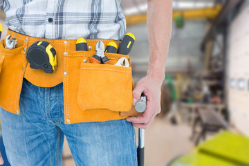Technician with tool belt around waist against workshop