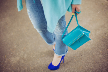girl is standing in jeans with a turquoise handbag and in blue high-heeled shoes in the street