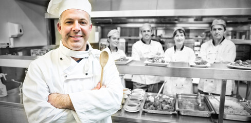 Fototapeta na wymiar Experienced head chef posing proudly in a modern kitchen with his team in the background