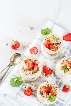 Healthy summer breakfast idea, homemade layered parfe dessert in small jar with granola, yoghurt and strawberry, dark background copy space