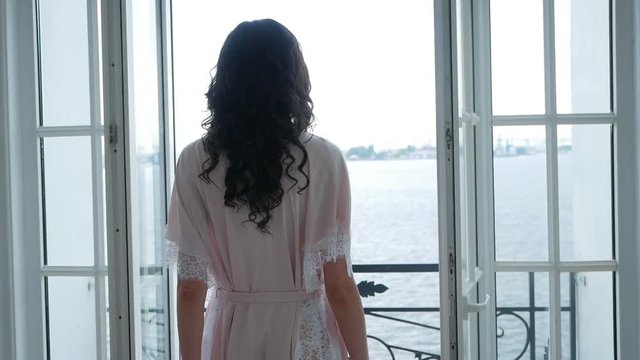 girl in pink light silk robe goes to the balcony to the window