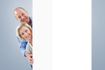 Mature couple smiling behind wall against grey vignette