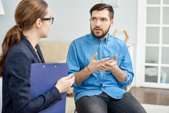Handsome bearded patient having lack of social skills trying to solve problem with help of highly professional psychologist, interior of cozy office on background