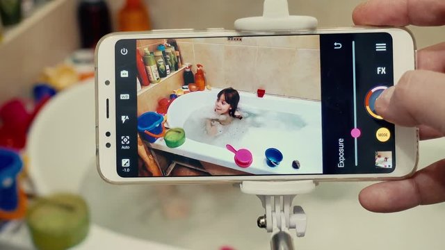 Happy dad taking a picture of his happy baby in bath with smartphone.