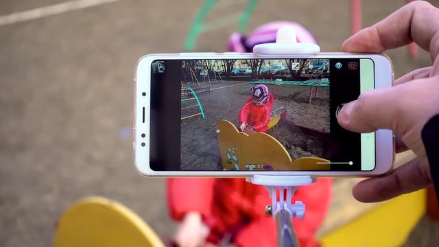 Parent is taking photo of her child on playground using phone.