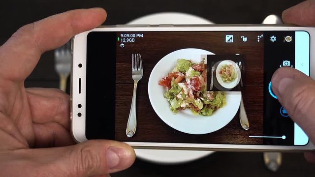 Vegetarian healthy food. Social networks smartphone photo. Man's hands takes phone photo of white plate with vegetables salad.