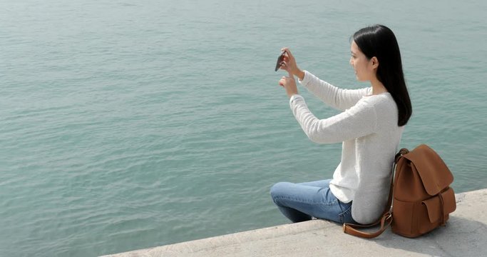 Woman taking the photo on cellphone with seascape
