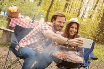 Smiling couple making selfie while making barbecue and having picnic day in the nature
