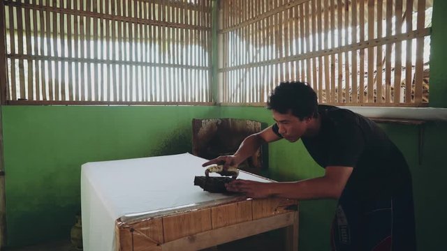 Adult indonesian man applying hot wax pattern to fabric using cap to make batik