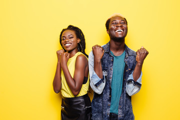 Fototapeta na wymiar Scream of win. Portrait of a happy young afro american couple screaming and celebrating isolated over yellow background