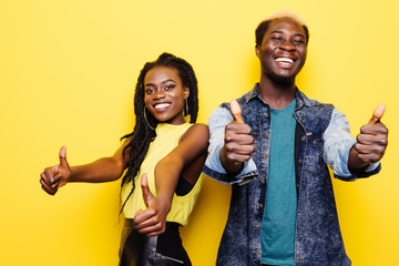 Good choise. Portrait of a smiling young afro american couple standing and showing thumbs up gesture over yellow background