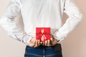 Young man hiding red gift box behind his back