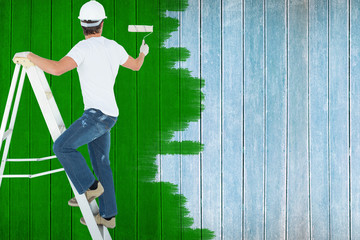 Man on ladder painting with roller against wooden planks