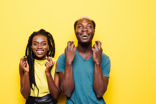 Portrait Of An Excited Young African Couple Standing Together And Cross Fingers Up At Copy Space Isolated Over White Background