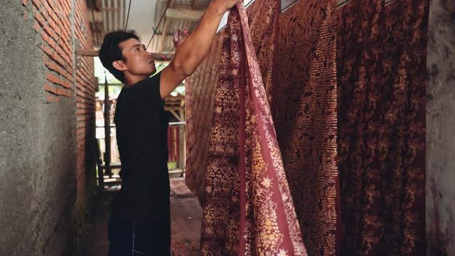 Adult indonesian man taking dried red dyed batik fabric from rope