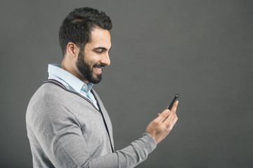 Bearded handsome happy man holding smartphone in hand on grey isolated background