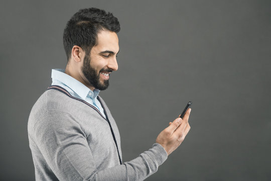 Bearded handsome happy man holding smartphone in hand on grey isolated background