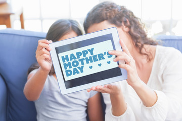 mothers day greeting against happy mother and daughter sitting on the couch and taking selfie