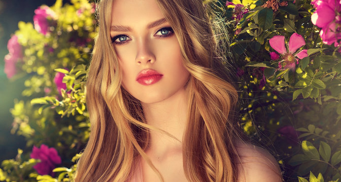  Beautiful spring model girl in flowers in summer blossom park. Woman in a blooming garden . Fashion, Cosmetics & Perfumes . Curly blonde hair 