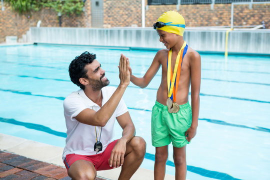 Boy giving high five to coach near poolside - Powered by Adobe