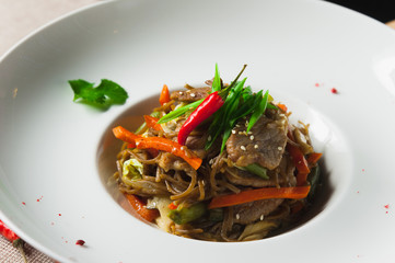 Healthy pasta with meat and vegetables on a white plate with with herbs and pepper