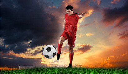 Football player in red kicking against green grass under blue sky