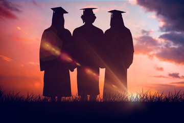 Three students in graduate robe holding a diploma against orange and blue sky with clouds