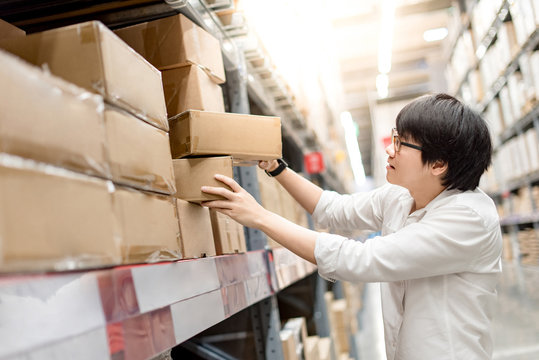 Young Asian man picking paper box from shelf in warehouse, shopping warehousing or packing products concepts