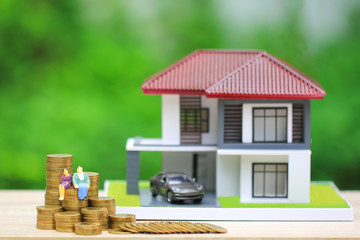Miniature couple standing on gold coins money with model house and car on natural green background, Save money for prepare in future and retirement concept.