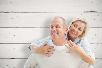 Happy mature man giving piggy back to partner against white wood