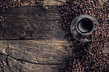 Cup of black coffee with beans on wooden table