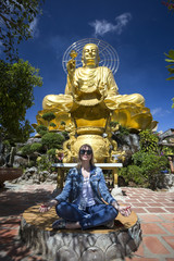girl sitting in the lotus position with a big golden Buddha on the background