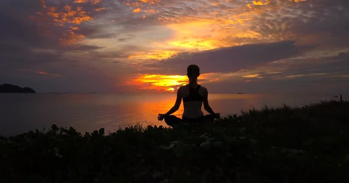Serenity and yoga practicing at sunset, camera slowly move around woman practice meditation sitting front to seaside at sunset or sunrise