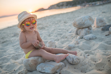 Portrait of caucasian child girl with sunglasses and hat sittng on sandy beach