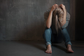 Sad young woman sitting at the wall. The young blonde. Depression and problems