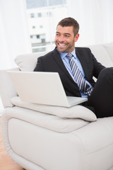 Smiling businessman on a sofa with a laptop