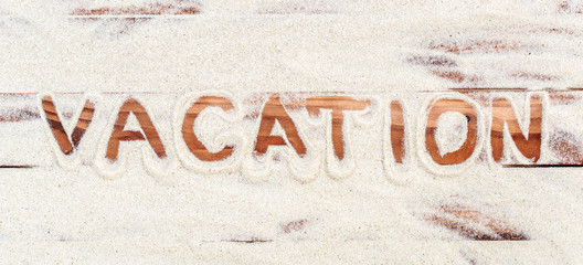 Word "vacation" written by sand on the wooden planks.