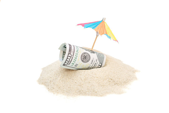 Rolled up money with beach umbrella on the heap of sand. Isolated on white.