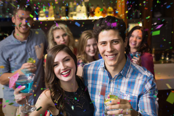 Happy friends drinking cocktails together against flying colours