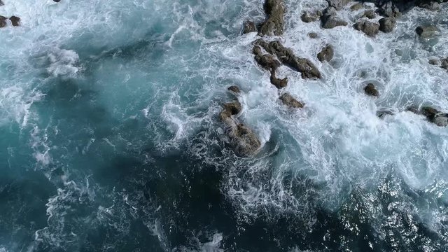 Aerial view of the sea roll onto black lava coast, top down shot with slow lifting up move