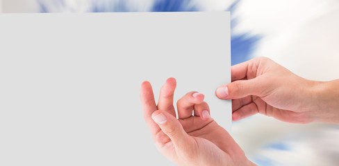 Hand showing card against blue sky with white clouds